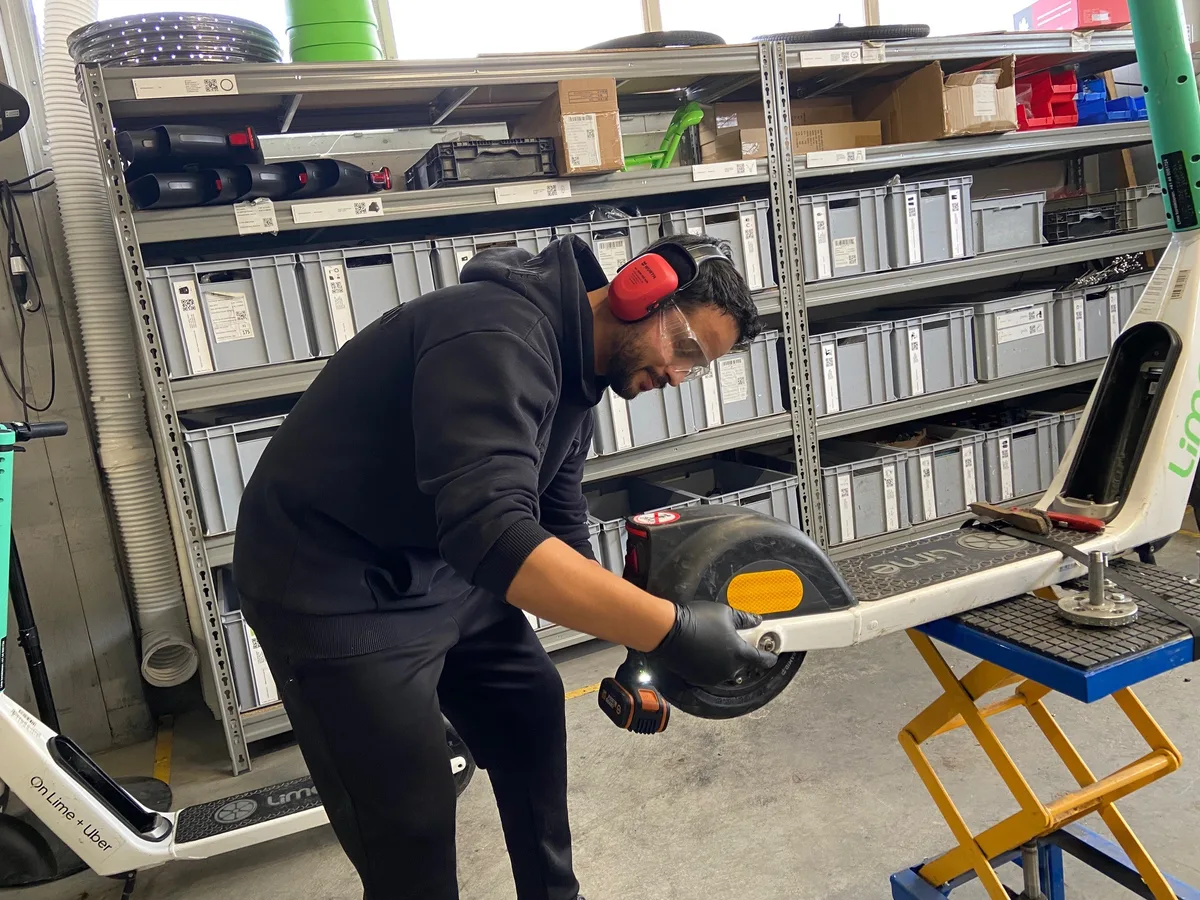 Ein Mann steht neben einem Lime-Fahrzeug und flickt den Reifen.